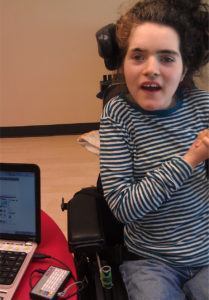 A young using the switches in a power wheelchair to scan through items on a laptop computer to make a selection.