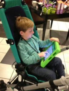 A little boy in a specialized stroller, activating buttons on an iPad for communication.