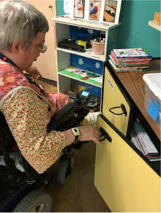 A woman in her wheelchair, opening a cupboard with handles adapted for easy-pull opening.