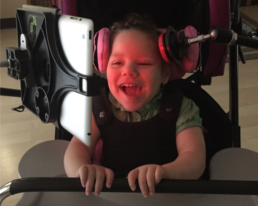 Little girl using a head switch to activate an iPad mounted in front of her.